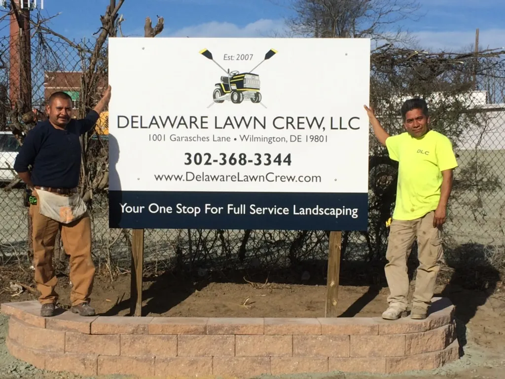 Two Delaware Lawn Crew team members beside the company sign in Wilmington, DE