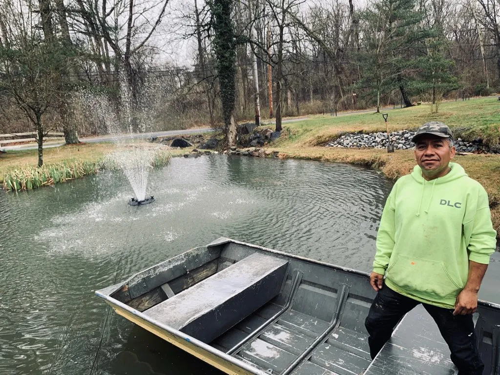 A Delaware Lawn Crew member beside a pond with an aeration fountain.