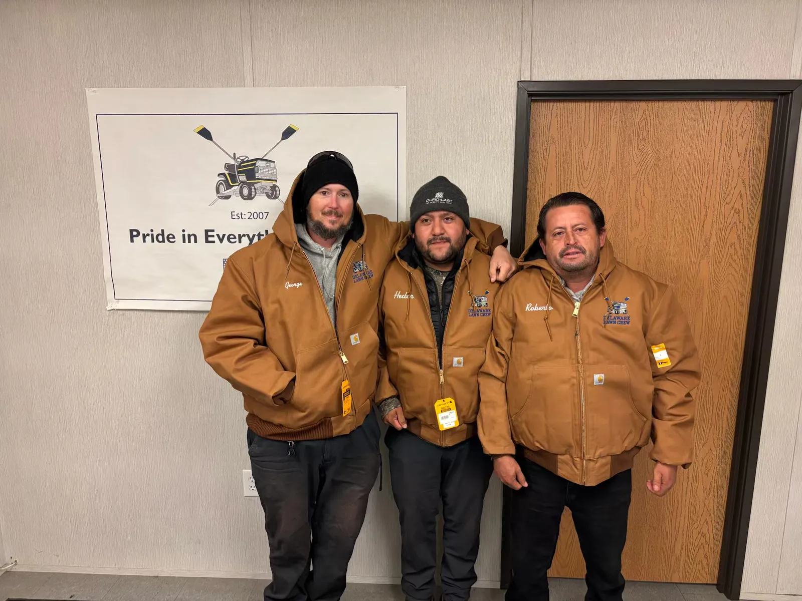 Three Delaware Lawn Crew members in branded jackets at the shop.
