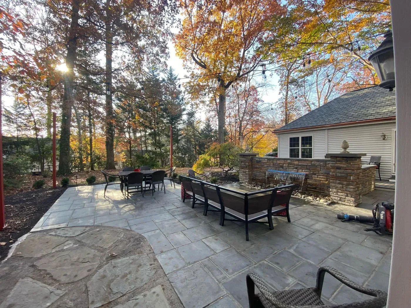 A large bluestone patio with a dining set and fire table in fall