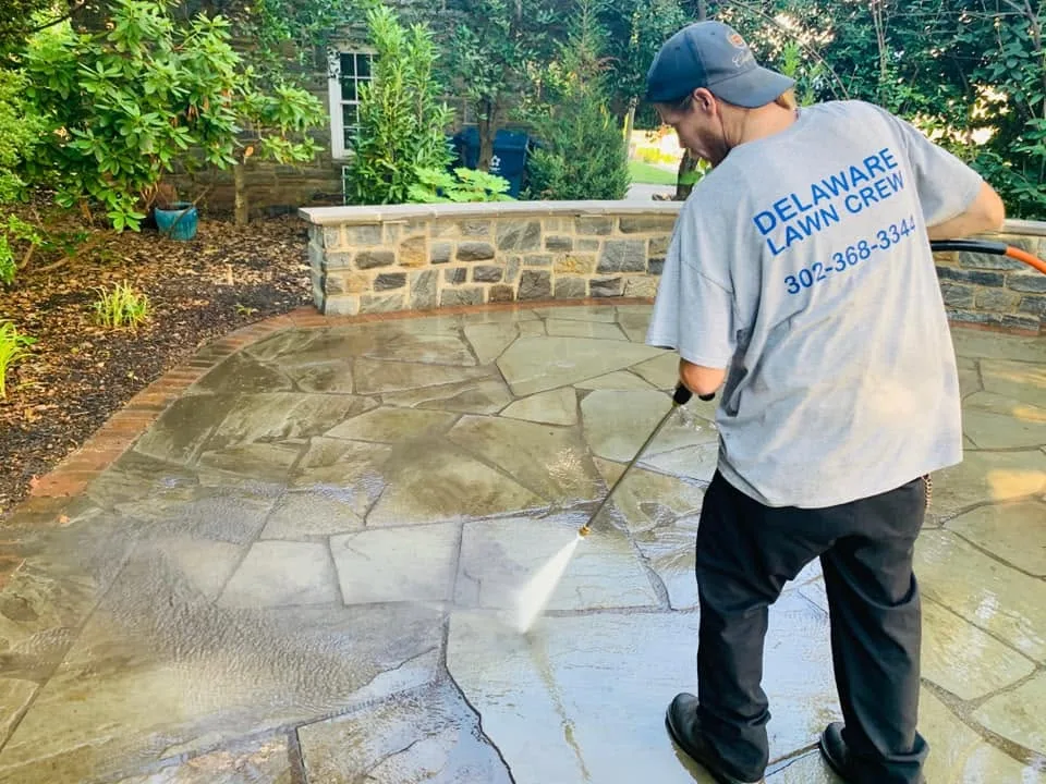 A Delaware Lawn Crew technician power-washing a flagstone patio in New Castle County.